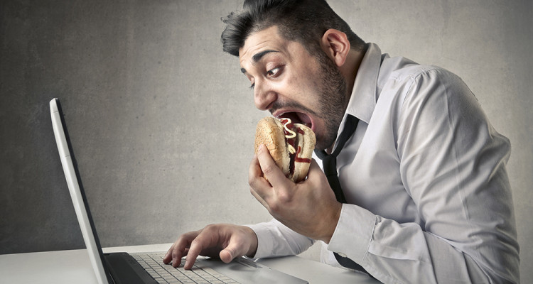 man eating burger while working